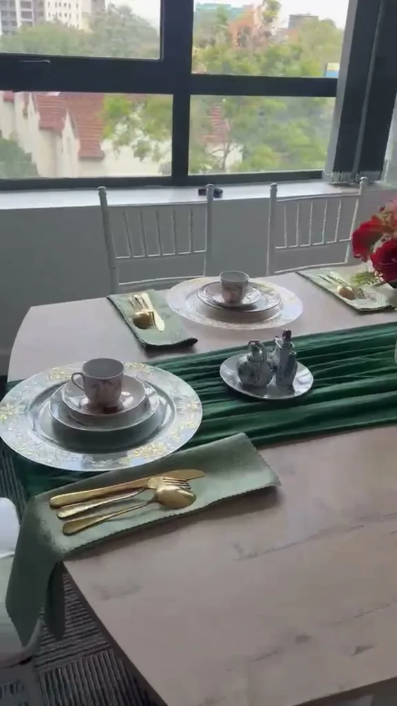 Vintage floral china teacup, saucer and plates stacked on a patterned glass charger with gold cutlery on a sage napkin, Nairobi rooftops through the window