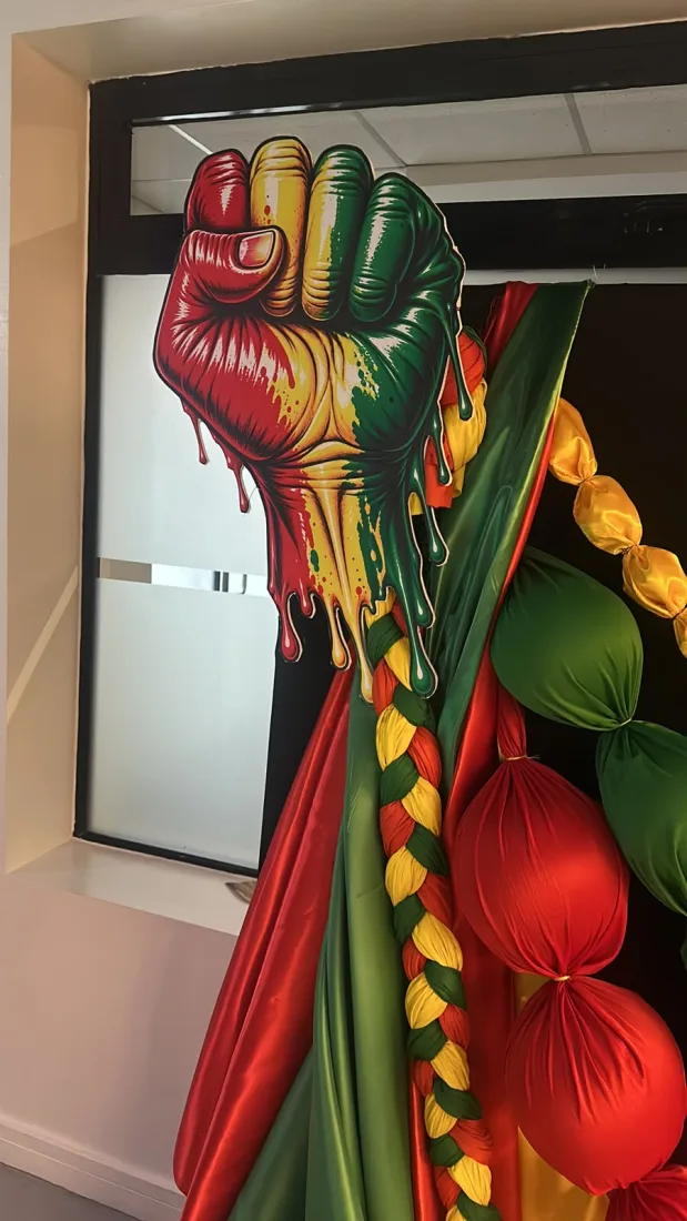 Large graphic fist backdrop in satin red, green and gold with braided trim and fabric ball garlands, set up as a photo corner