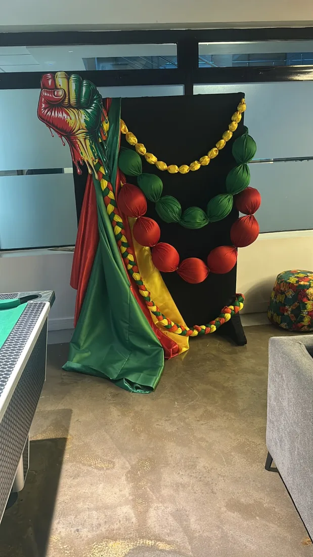 The red, green and gold fist backdrop set up in a office lounge corner alongside a pool table and seating