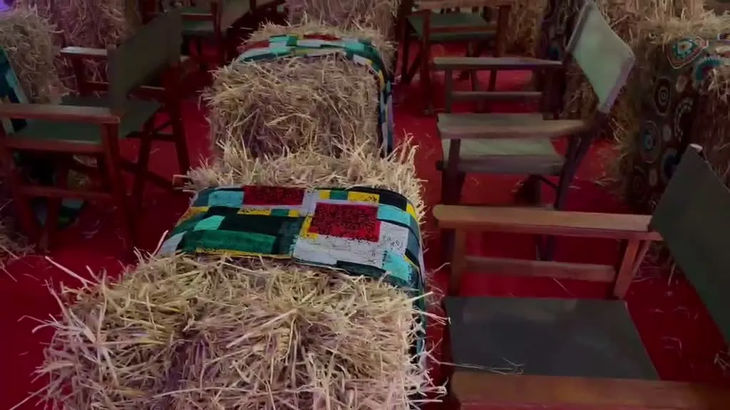 Two hay-bale seats upholstered in colourful kitenge patchwork cushions in black, green, red and yellow, with director's chairs alongside on a red carpet