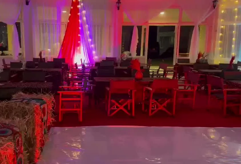 Dome tent interior lit in red, purple and teal with hay-bale seating, dressed dining tables, director's chairs and a dance floor down the middle