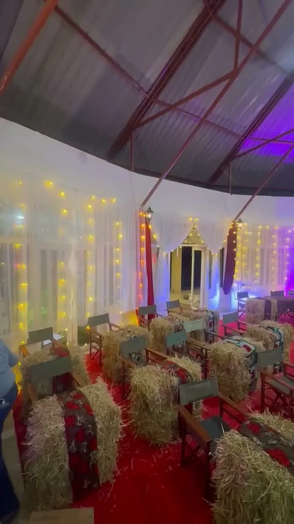 Rows of dressed hay-bale seating in front of fairy-light curtain walls and a red-draped triangular light feature inside the dome tent